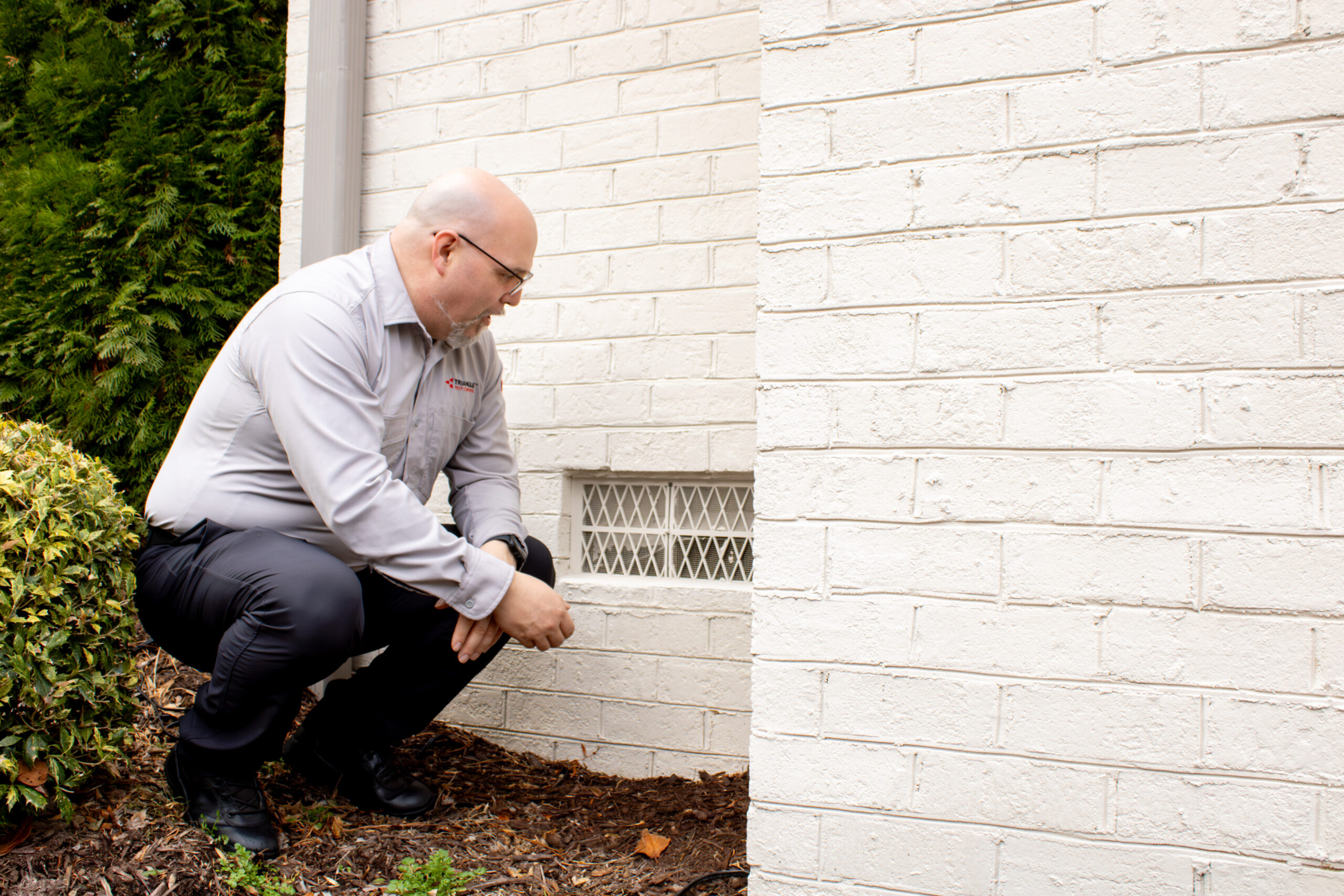 Pest control technician inspecting crawl space vent at Raleigh home before spring
